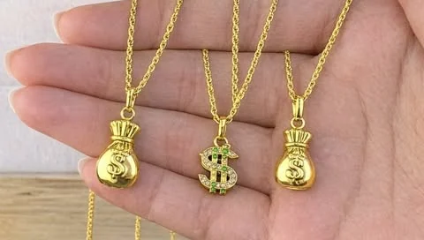 Tres cadenas finas de oro con dijes sostenidas en la palma de una mano.