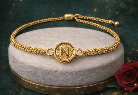 Pulsera tejida en oro de 18 quilates con medallón de inicial, sobre un pedestal de terciopelo.