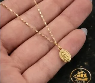 Cadena fina de oro con una medalla oval descansando en la palma de una mano.