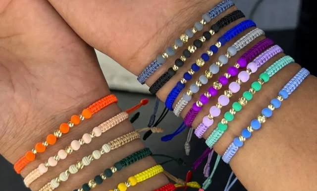 Pulseras tejidas de colores vivos con balines de oro, apiladas en una muñeca.